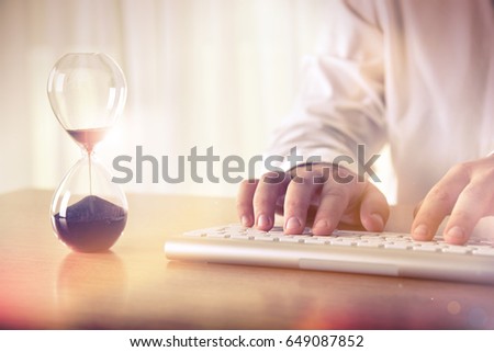 Man's hands typing on computer keyboard next to a hourglass. Concept of time management, business schedule and deadline, for background, website banner, promotional materials, advertising. Royalty-Free Stock Photo #649087852
