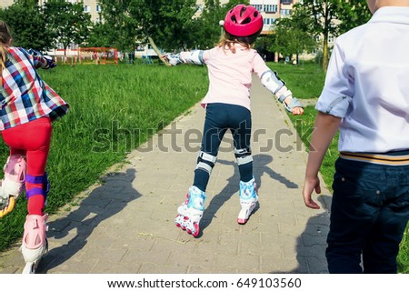 The girl learns to skate on the street. Children wear protective pads and a protective helmet for safe riding on rollers. Active sports activities for children