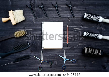 Hairdresser tools on wooden background. Blank card with barber tools flat lay. Top view on wooden table with scissors, comb, hairbrushes and hairclips with empty notebook and pencil, copy space