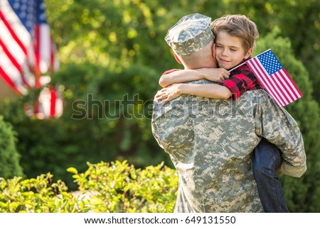 American soldier reunited with son on a sunny day with american flag on the background