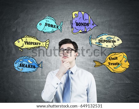 Pensive businessman wearing glasses and a white shirt with a tie is standing near a blackboard with business buzzwords written on fish of different colors.