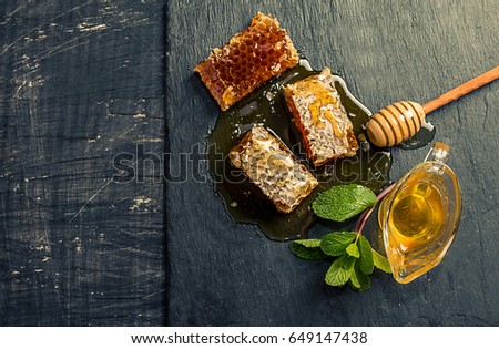 Honey, honeycomb, mint and honey dipper on black slate tray over grunge dark backdrop, top view