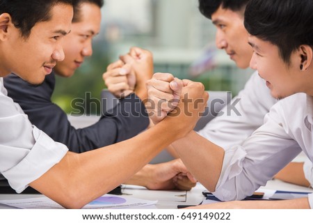 Business competition concept - Side view of serious asian employees sitting in two rows and doing arm wrestling. selective focus