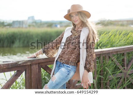 woman in straw hat staying near the wooden fence situated on the lake with a green sedge on the bank
