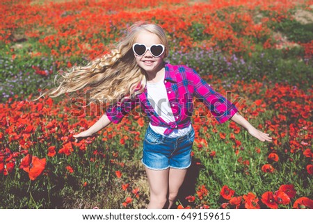 Child girl is wearing sunglasses and casual fashion clothes in spring field with bouquet of poppies