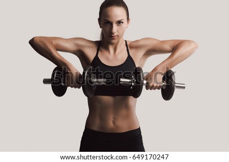 Beautiful young woman in a workout gear lifting dumbbells Royalty-Free Stock Photo #649170247