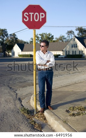 A man leaning leisurely against a stop sign at the corner of a quite intersection.
