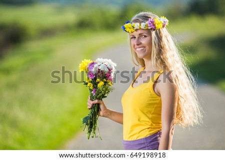 Beautiful blonde girl holding bouquet of flowers at the country road.Woman enjoys in nature