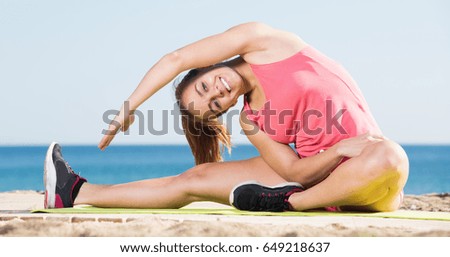 Happy young sportwoman doing gymnastics at sea beach on summer day