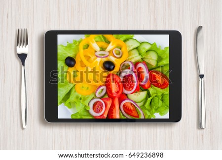 black tablet pc with healthy food on screen and wooden table