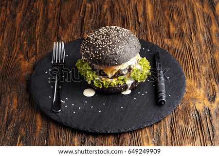 black burger with beef cutlet with vegetables, sesame, oil shale on the board on a dark background