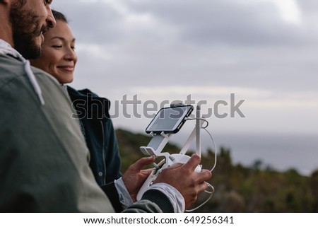 Couple using aerial drone for photography. Man and woman standing in countryside taking photo on flying drone during vacation.