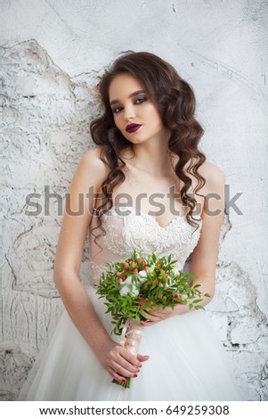Portrait of a beautiful young girl of European appearance in a stylish white wedding dress with a hairdo and makeup with a wedding bouquet in the hands of fine flowers