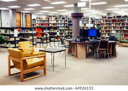 Computer station at the university college library with seating area in the foreground. One young female student searching far in the background.
