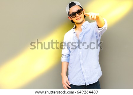 Portrait handsome young man. Attractive handsome cool guy is pointing finger to some favorite thing that makes him satisfied and happy, smile face. He wears jeans. beautiful sunlight background, space