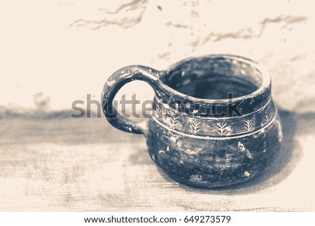 Old vintage photo. Old clay mug stands on a wooden surface near a white brick wall