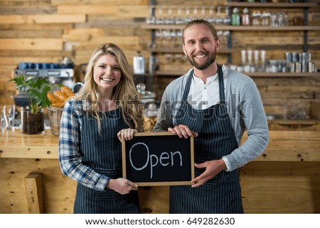 Portrait of waitress and waiter standing with open sign board in cafe