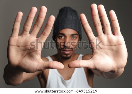 Picture of young african man isolated over grey background. Looking at camera showing hands to camera.