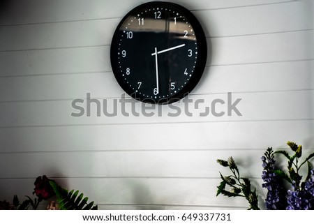 Time,Black clock hanging at the white wall.White wall decoration with a picture frame, clock and plants