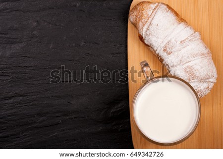one croissant sprinkled with powdered sugar on black stone background with copy space for your text. Top view