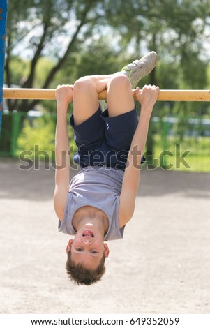 A teenager in a T-shirt is engaged in gymnastics on a horizontal bar.