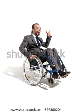 excited disabled businessman in wheelchair showing rock sign isolated on white