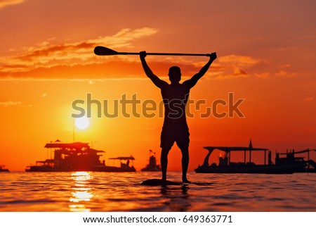Paddle boarder. Black sunset silhouette of young sportsman on stand up paddleboard. Water sport activity, SUP surfing in adventure camp on active family summer beach vacation.