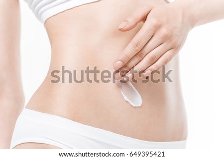 Close-up partial view of woman in underwear applying body cream on belly 