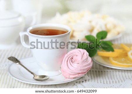 Cup of hot tea with pink marshmallow and lemon on a white table
