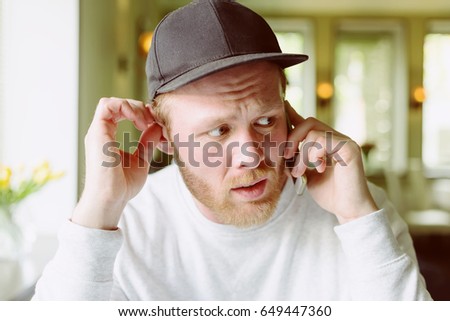 Fashionable and stylish young man talking on the phone at the cafe. Blurred background. Film effect.