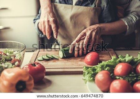 Cropped image of grandma and granddaughter cutting cucumber while preparing salad in kitchen