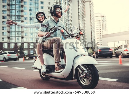 Beautiful young couple in sun glasses and helmets is smiling while riding a scooter Royalty-Free Stock Photo #649508059