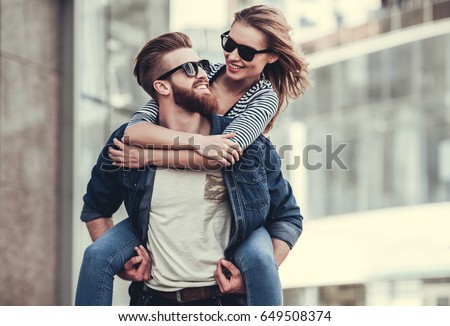 Beautiful young couple in sun glasses looking at each other and smiling while standing outdoors. Girl piggyback Royalty-Free Stock Photo #649508374