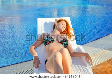 Leisure time. Beautiful young woman lying on the deck chair near the pool