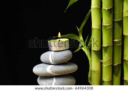  Burning candle on stones with bamboo grove on black background