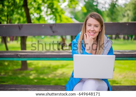 Beautiful student woman is using a laptop and sitting on a bench in the university campus. 