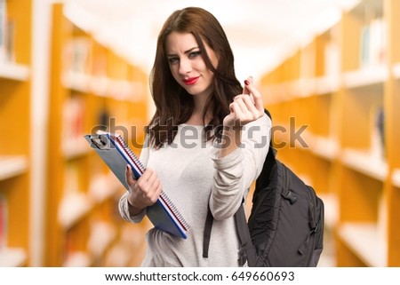 Student woman making money gesture in a library