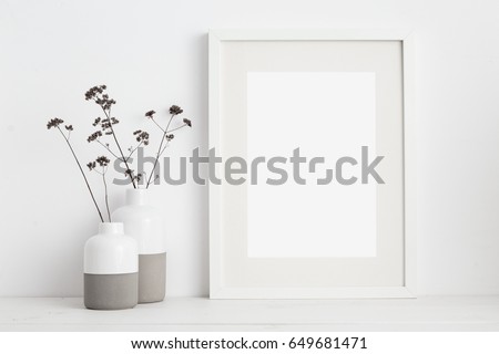 Mock up white frame and dry twigs in vase on book shelf or desk. White colors. Royalty-Free Stock Photo #649681471