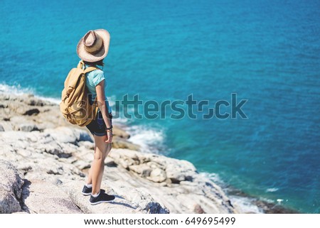Young european female tourist with a backpack and bamboo cowboy style hat looking at the sea while standing on the view point with the scenic beauty landscape. Copy space for your text.