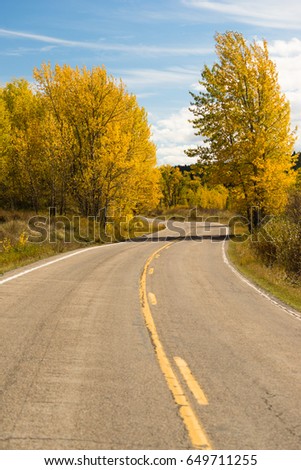 A well worn two lane road leads around a bend Autumn season fall color