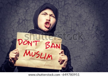 Muslim girl in black hijab holding a poster with an inscription DON'T BAN MUSLIM on the background wall with cracks