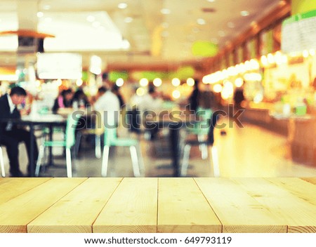 Food court or food center in shopping mall. Interior consist of table, restaurant, coffee shop. Busy with  people to buy food, sitting, eating. Wood table top for product display or blurred background