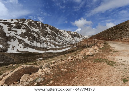 Mountain landscape with winding road and peaks covered by melting snow shot on sunny day