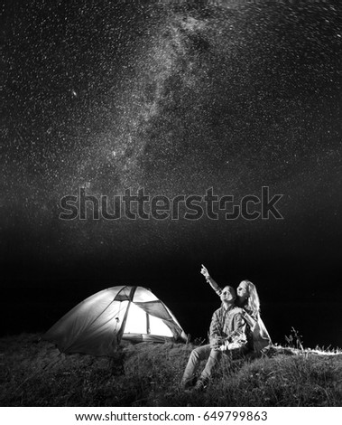 Tourist couple - girl and guy looking at the shines starry sky at night. Pair sitting near camping. Black and white
