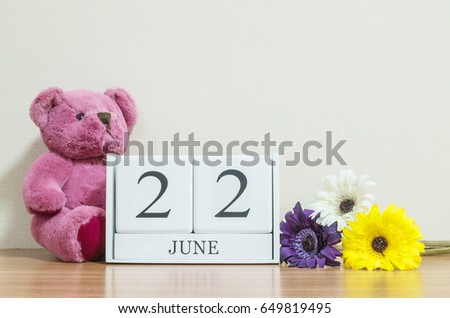 Closeup surface white wooden calendar with black 22 june word on brown wood desk and cream color wallpaper in room textured background with copy space in selective focus at the calendar