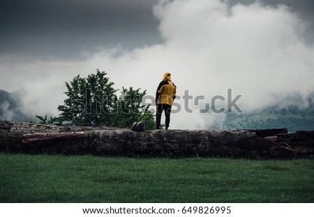 Traveler man standing on a tree trunk in a rainy day in mountains