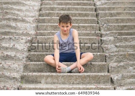A teenager in a T-shirt sits on concrete steps.