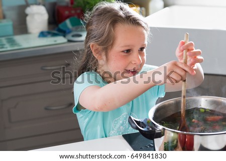 Portrait of a little girl cooking a recipe in the kitchen with her mother. She stirs the contents of a saucepan with a spoon