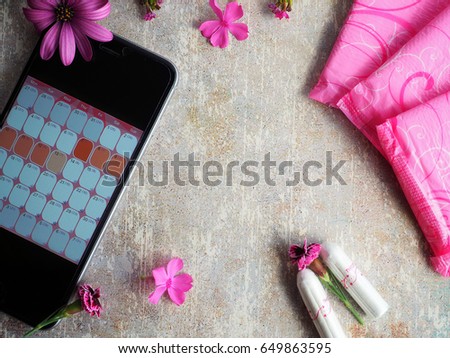 Woman hygiene protection during menstruation. Close up cotton tampons, pink menstruation pads, pink flowers and mobile phone with menstruation calendar on vintage table.