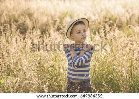 handsome boy stands in the grass field, a warm summer background behind him